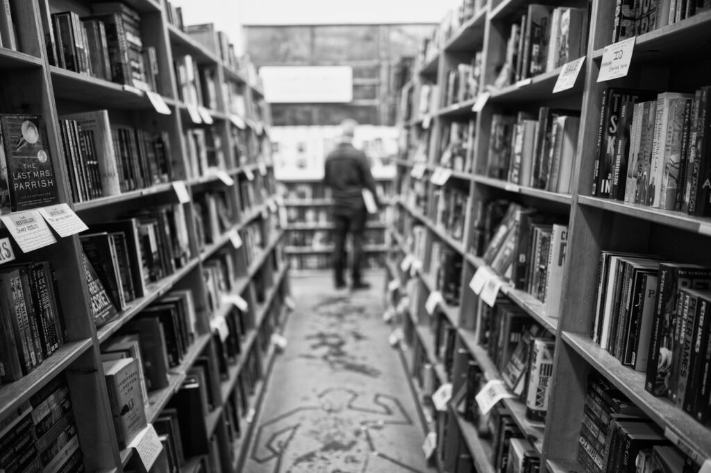 grayscale photo of man standing in front of books